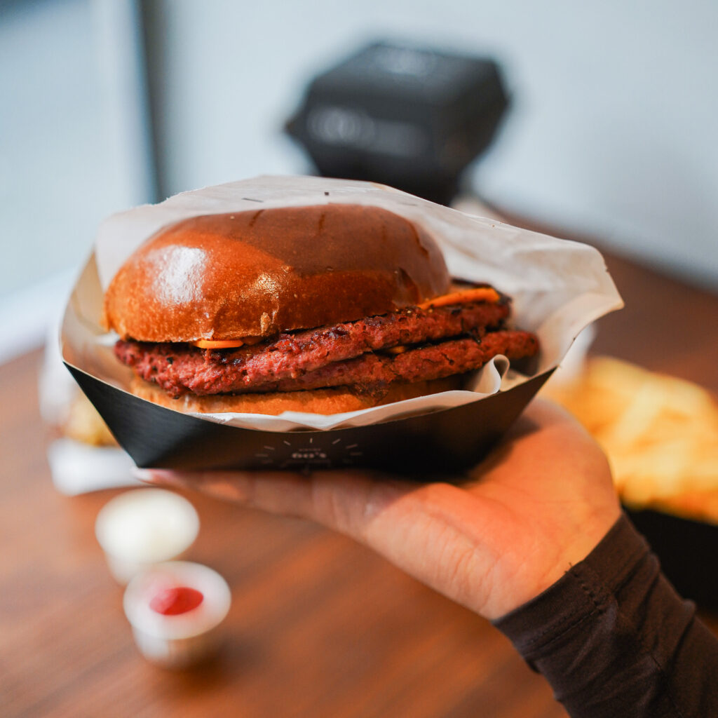 Ein saftiger Doppel-Patty-Burger in einem weichen Brioche-Bun, serviert in einer schwarzen Box und gehalten in einer Hand